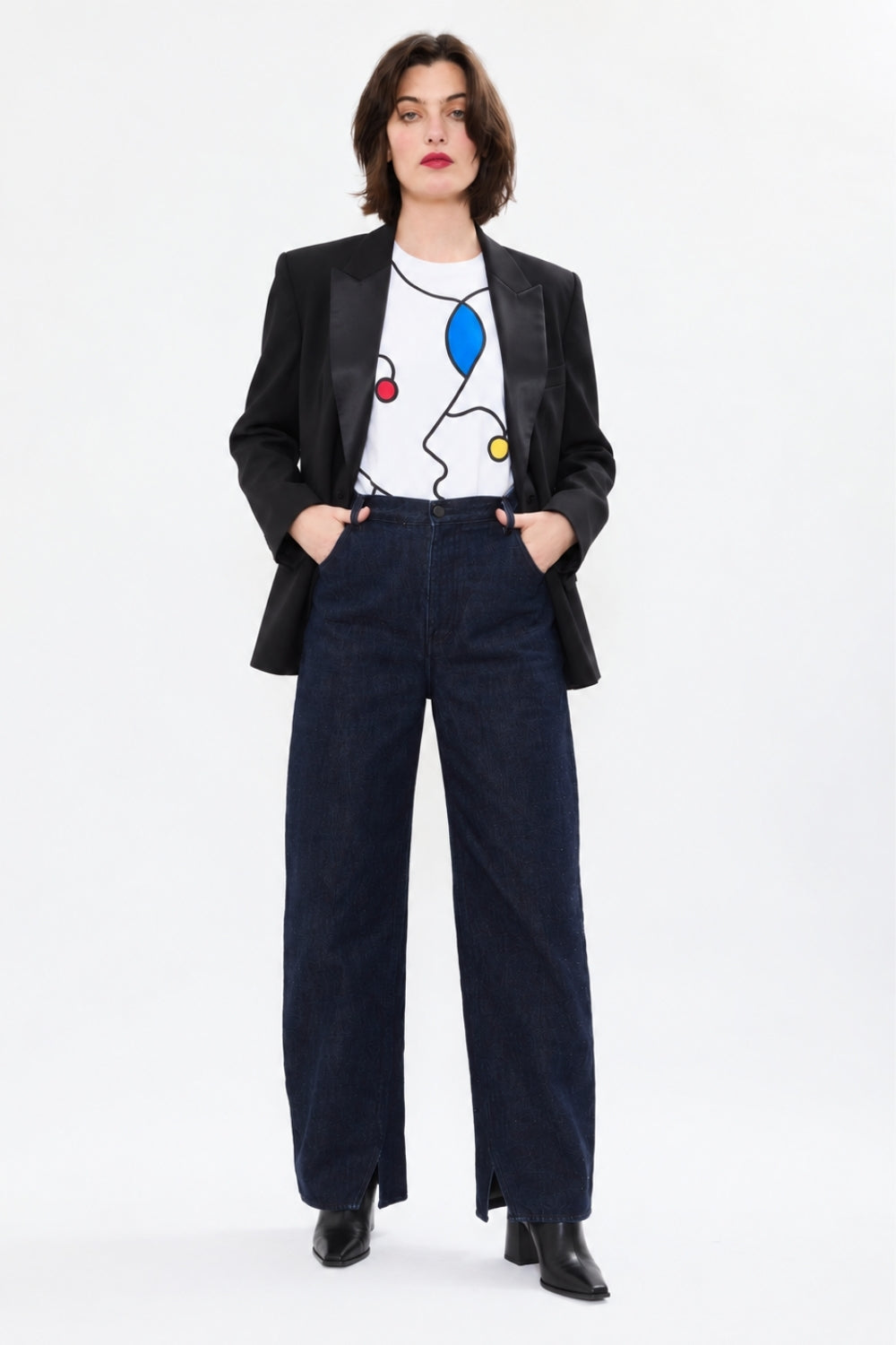 Model wearing AYT Studio LINE ART white organic cotton T-shirt featuring an exclusive REMED print, styled with a black tuxedo blazer, dark wide-leg jeans and black ankle boots.