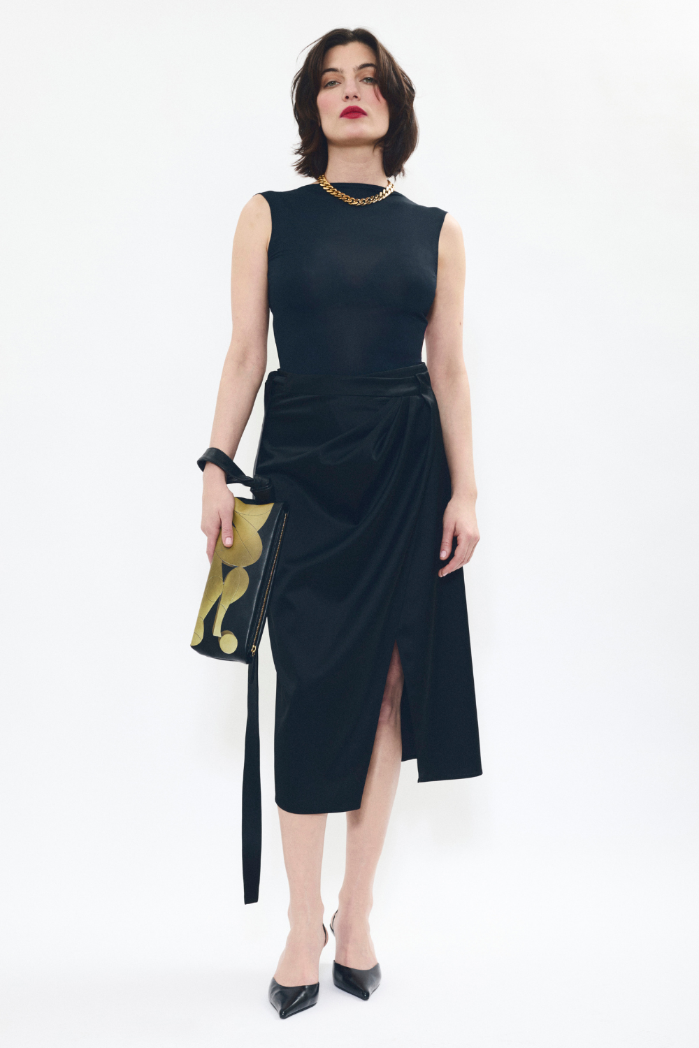 Model styling AYT Studio LIEN elongated black and gold leather pouch with an inspired artistic print and a scarf-inspired wrist strap.