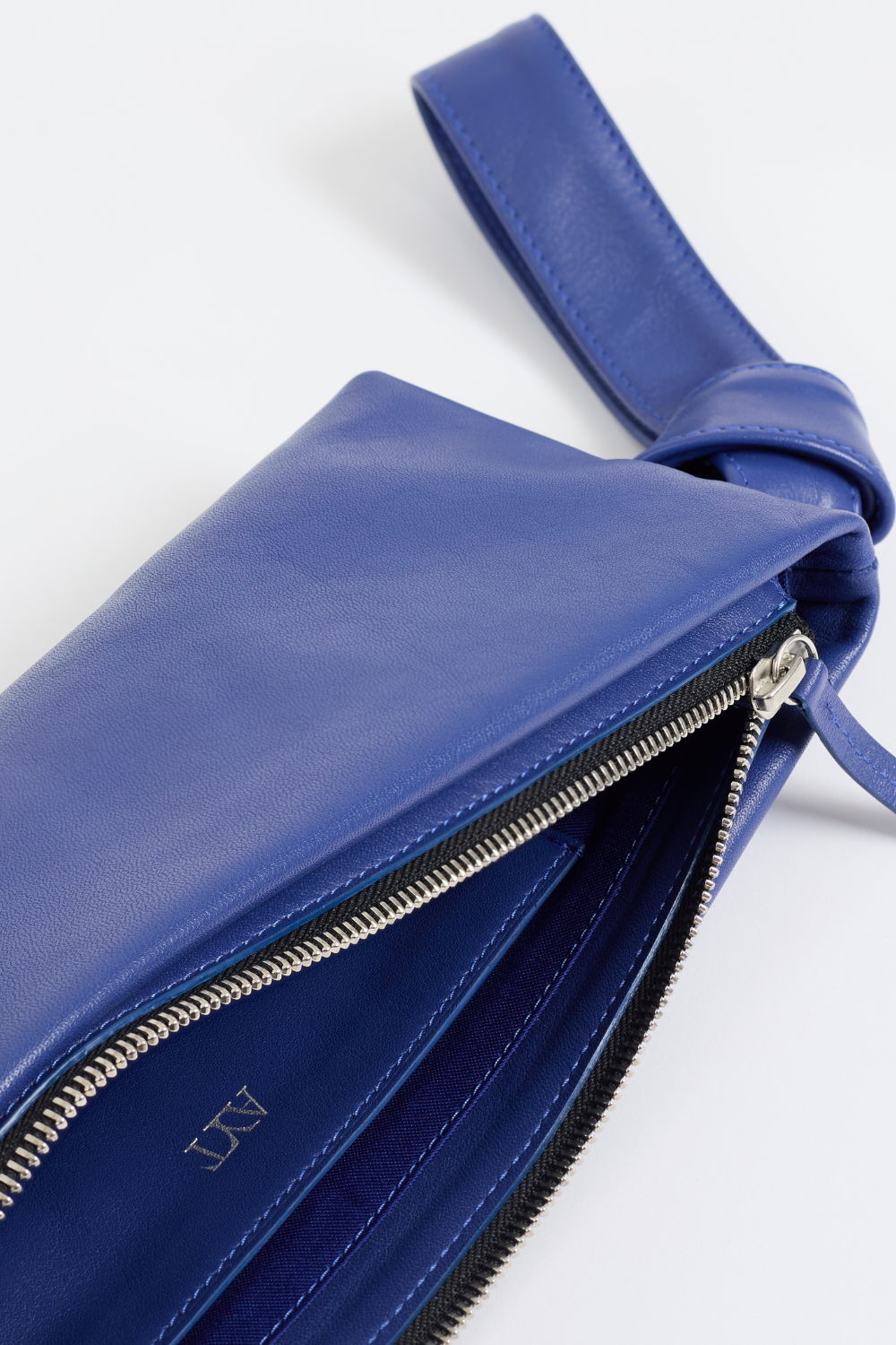 Details of Front view of AYT Studio 'LIEN' elongated leather pouch in smooth blue leather with knotted scarf-inspired wrist strap
