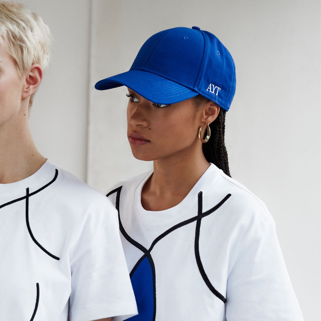 Two models wearing AYT Studio t-shirts with blue and black designs, one model wearing AYT Studio Signature Cap in blue with white embroidered 'AYT' logo and curved brim