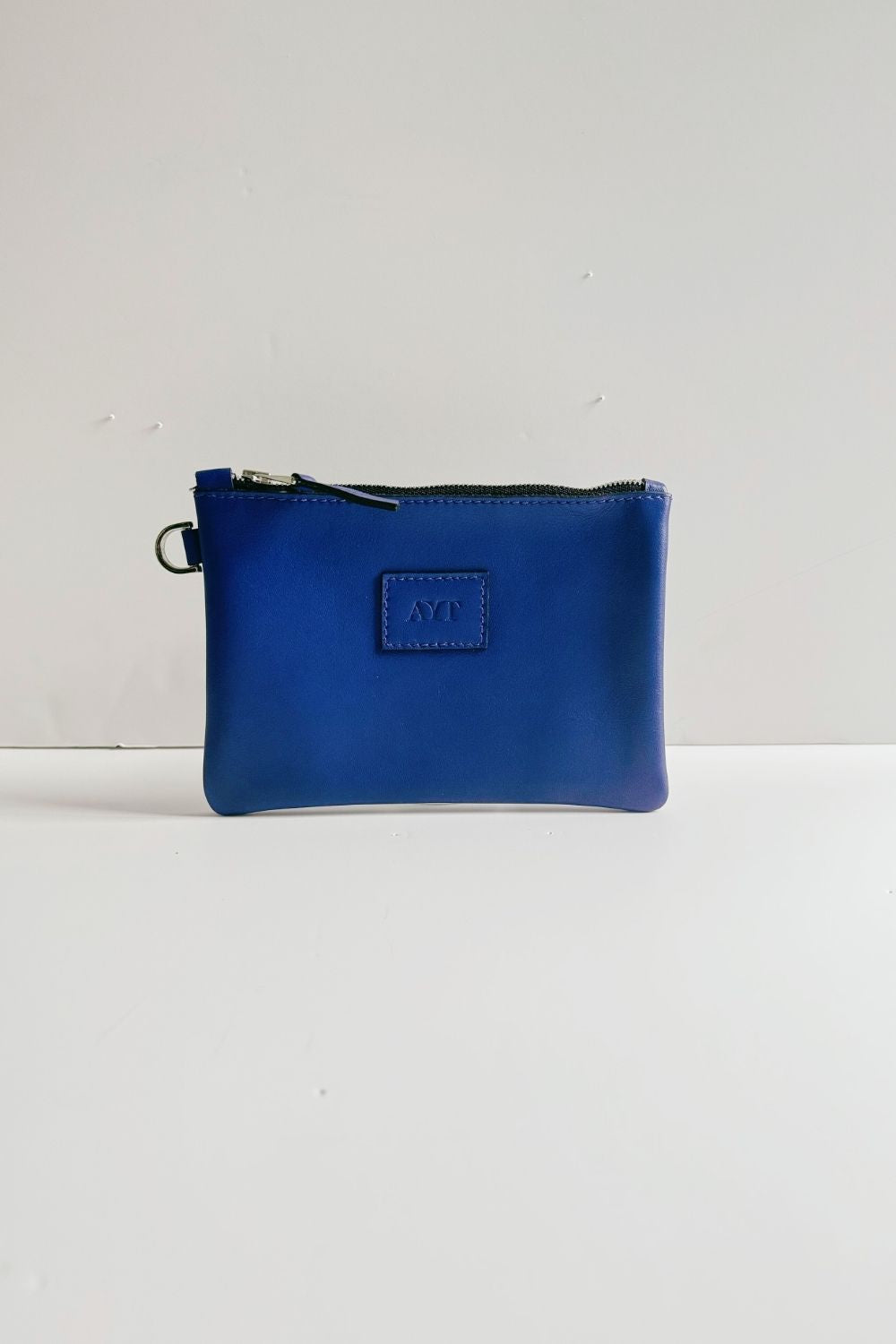 Front of handcrafted AYT Studio small leather pouch in blue with silver zipper and small brand logo