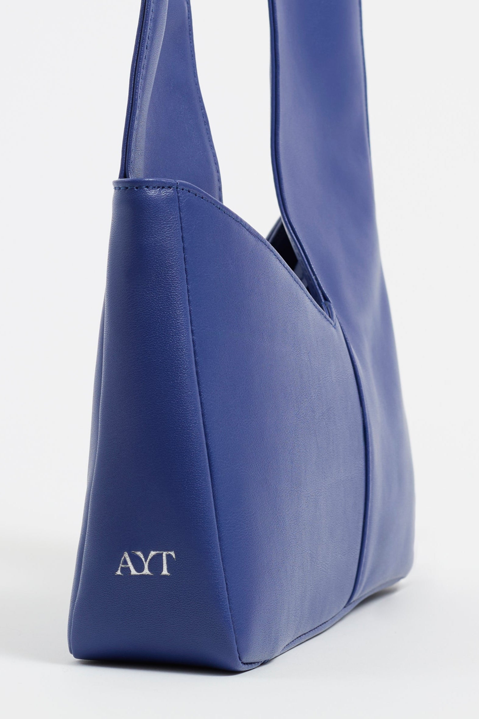 Side view of AYT Studio 'Dual' tote bag made of blue Italian leather and lining with full-length zipper, handle with sophisticated scarf detail, and white 'AYT' branding