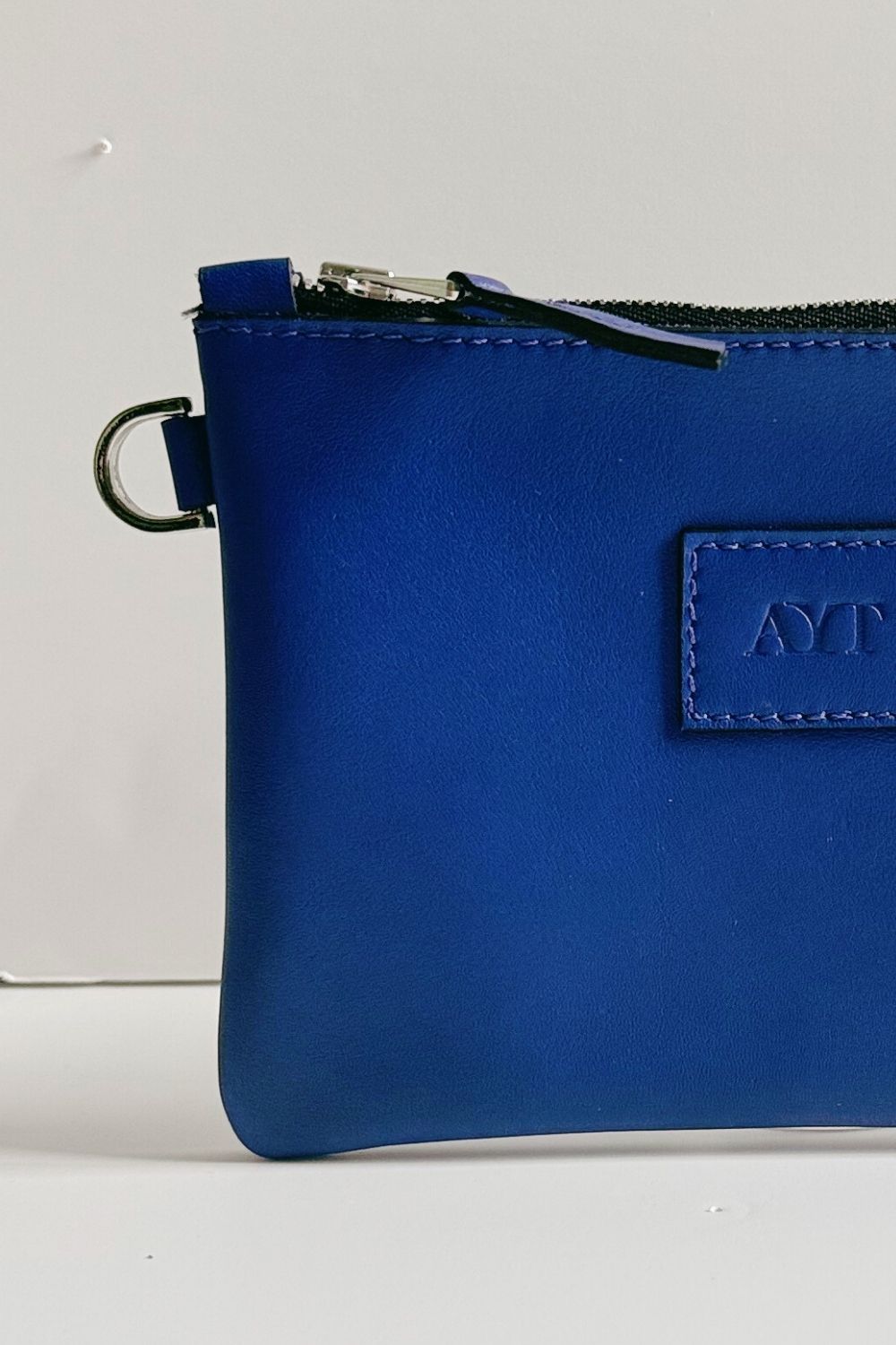 Details of handcrafted AYT Studio small leather pouch in blue, silver zipper, small brand logo with AYT embossing, U-ring