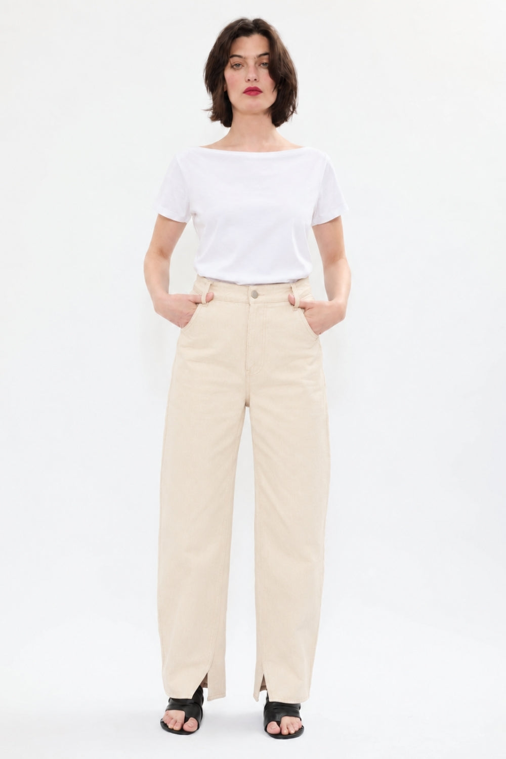Model styling AYT STUDIO 'TRIBE' high-rise curved straight leg 100% recycled cotton jeans in cream with signature blue AYT Studio logo, ankle slit detail, and functional front and back pockets.