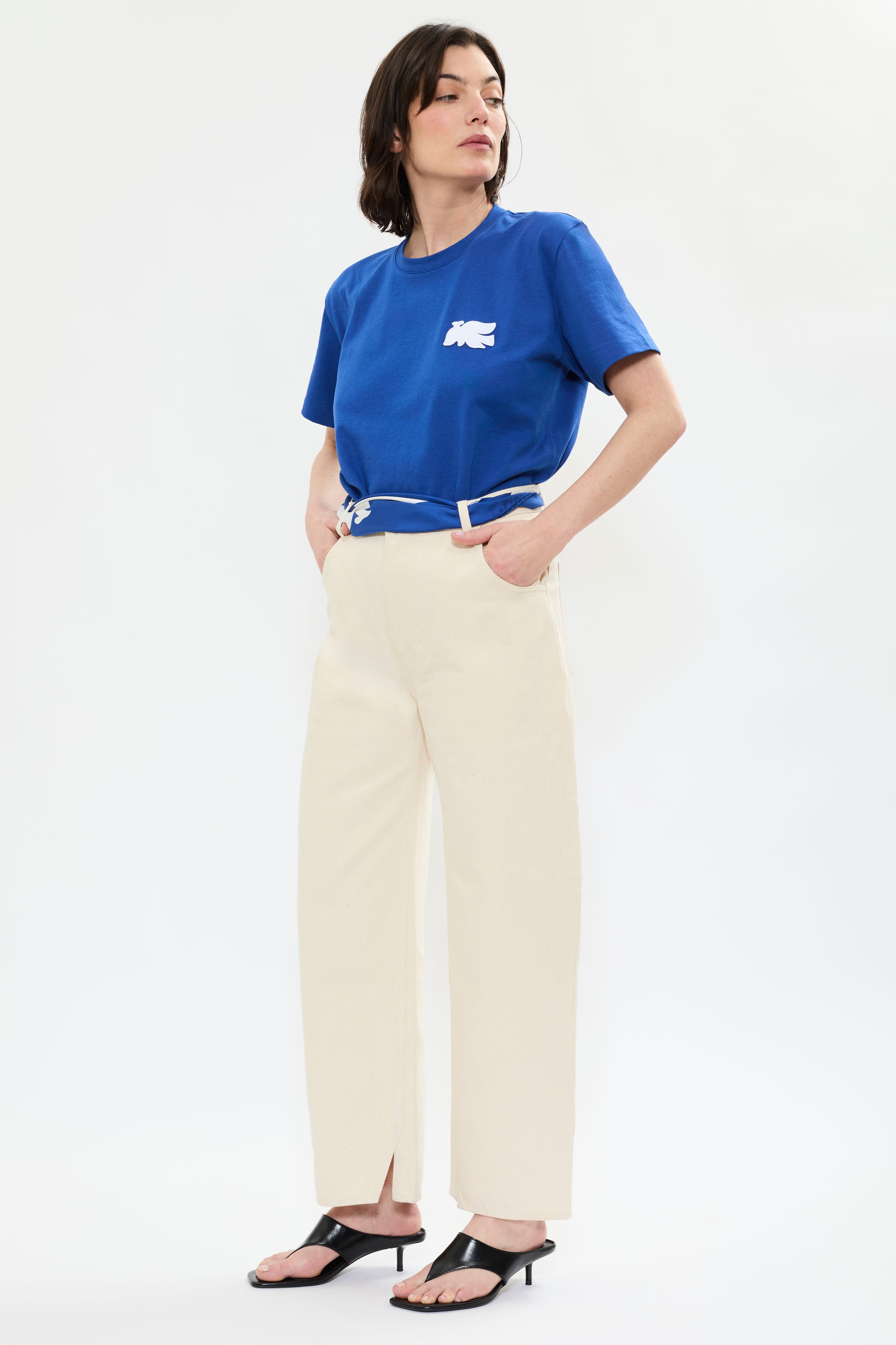 Profile of AYT STUDIO 'TRIBE' high-rise curved straight leg 100% recycled cotton jeans in cream with signature blue AYT Studio logo, ankle slit detail, and functional front and back pockets.