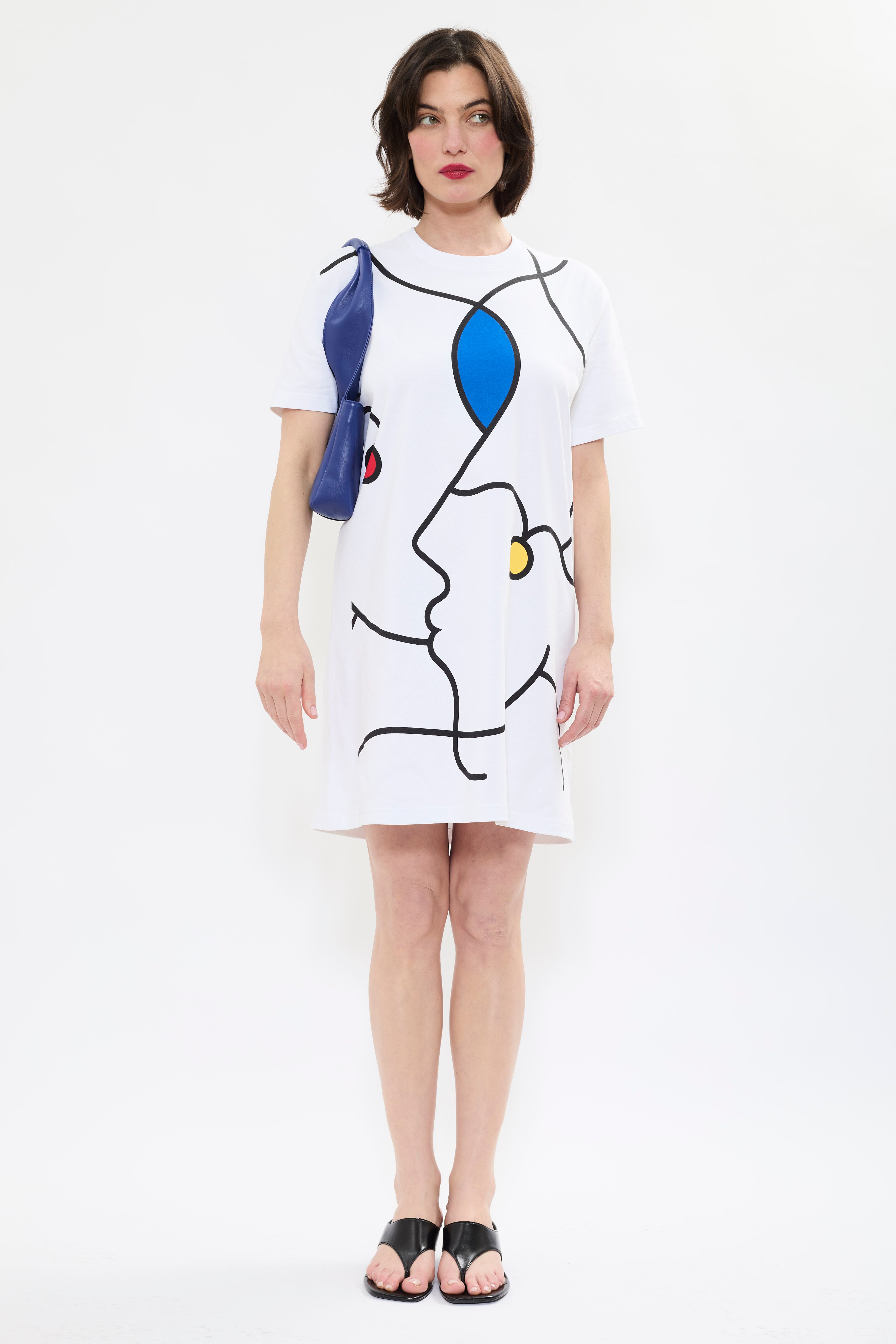 Front view of model wearing AYT Studio x Remed white organic cotton T-shirt dress with line-art print and a straight, oversized fit styled with AYT Studio 'DUAL' shoulder bag.