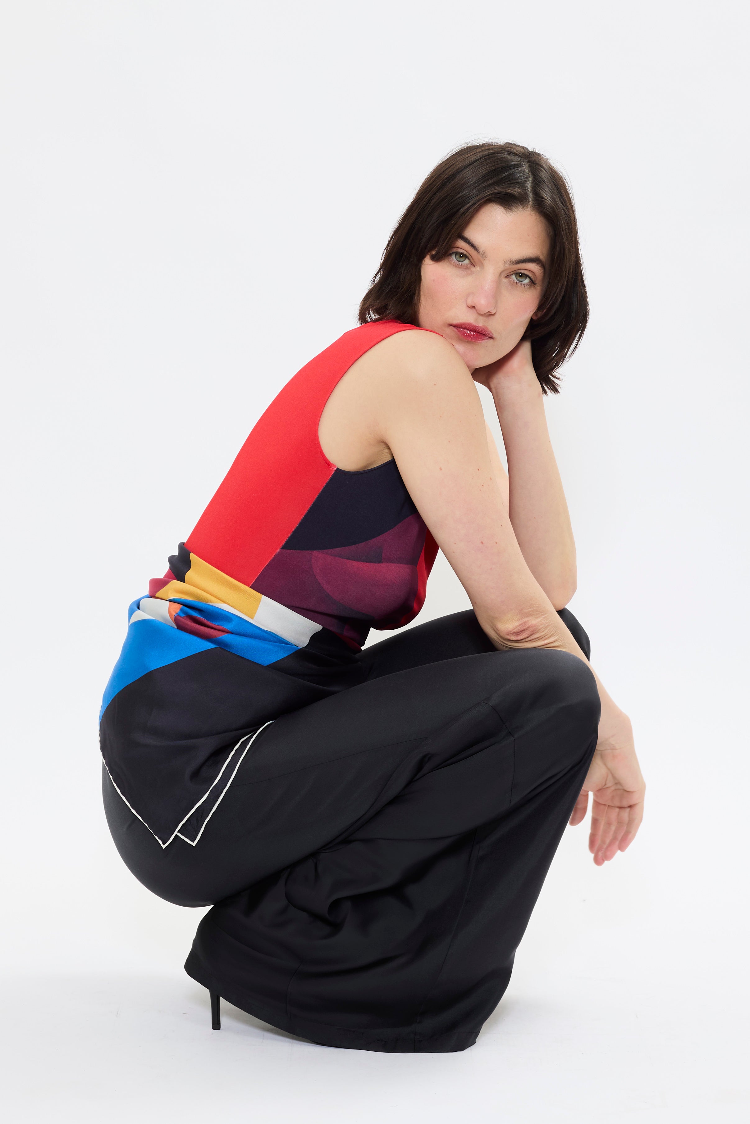 Model styling AYT STUDIO X REMED 'MUSE' tank top in deep reds and black with a fitted, sleeveless silhouette, and boat neckline that highlight the elegance of the cut with a bold artistic print.