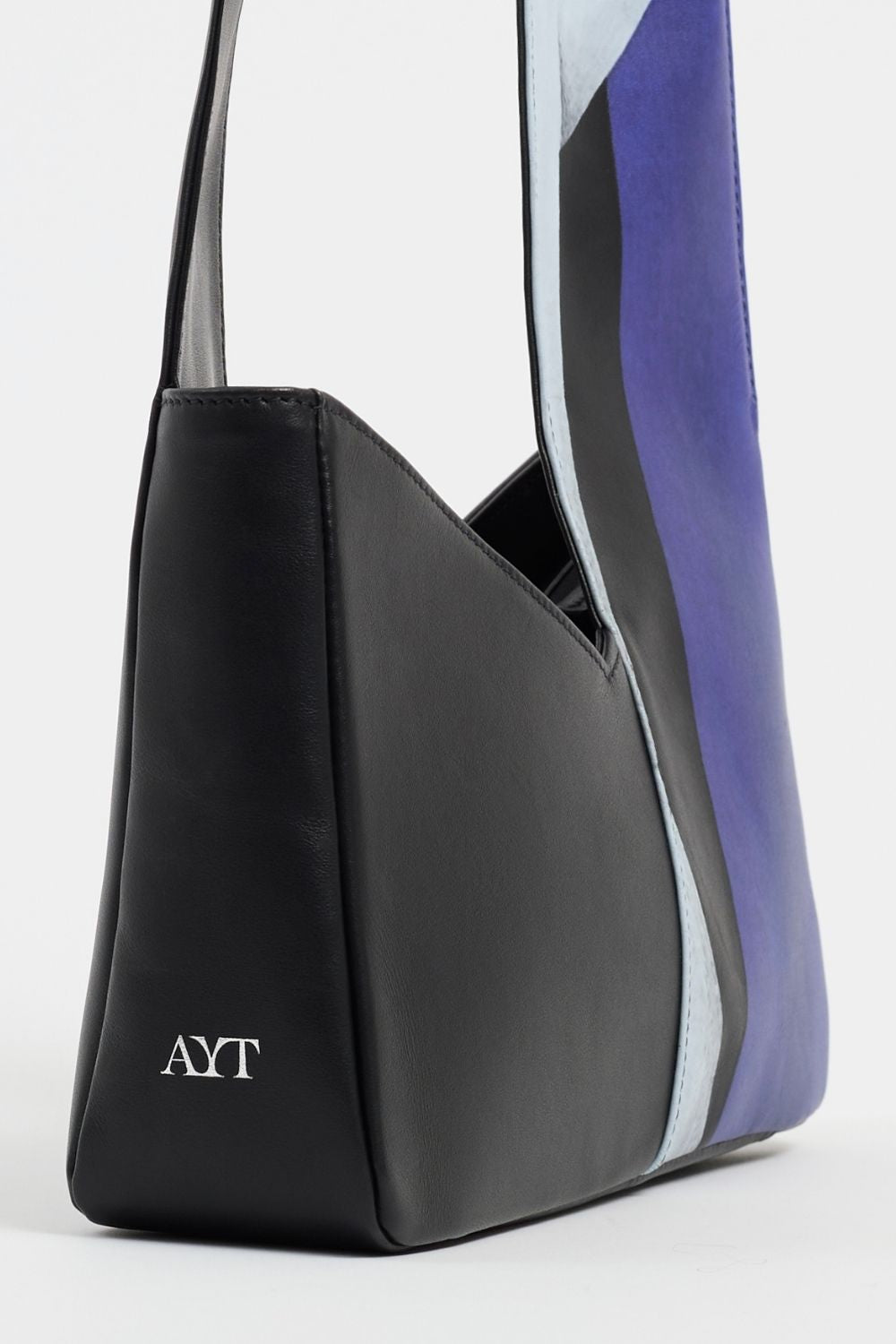 Side view of AYT Studio x Remed 'TEMPERANCE' shoulder bag made of black printed leather and blue canvas lining with zipped pockets, asymmetrical scarf-style handle, and 'AYT' branding