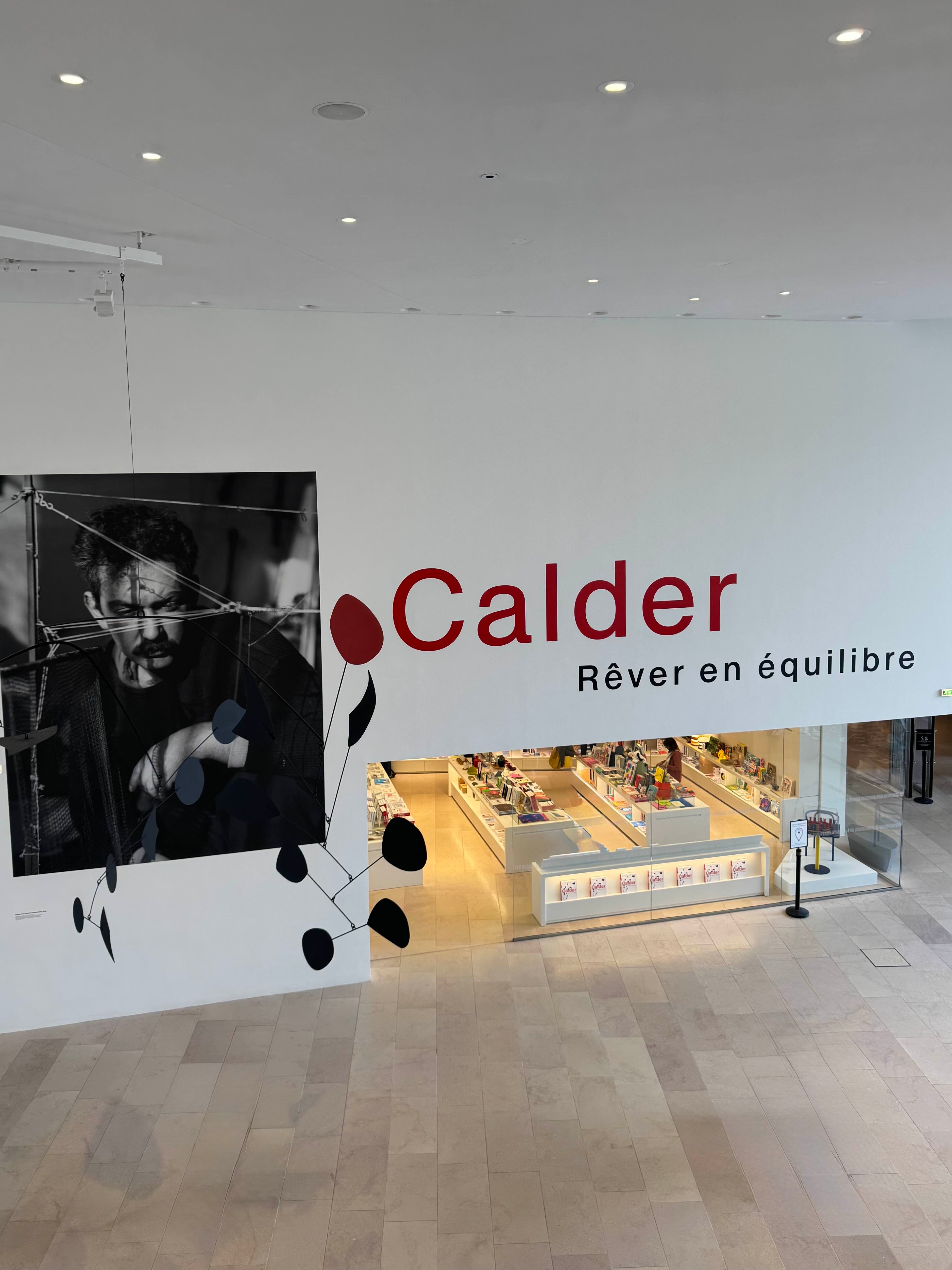 Museum interior with 'Calder' exhibit featuring a black and white portrait and abstract sculpture.