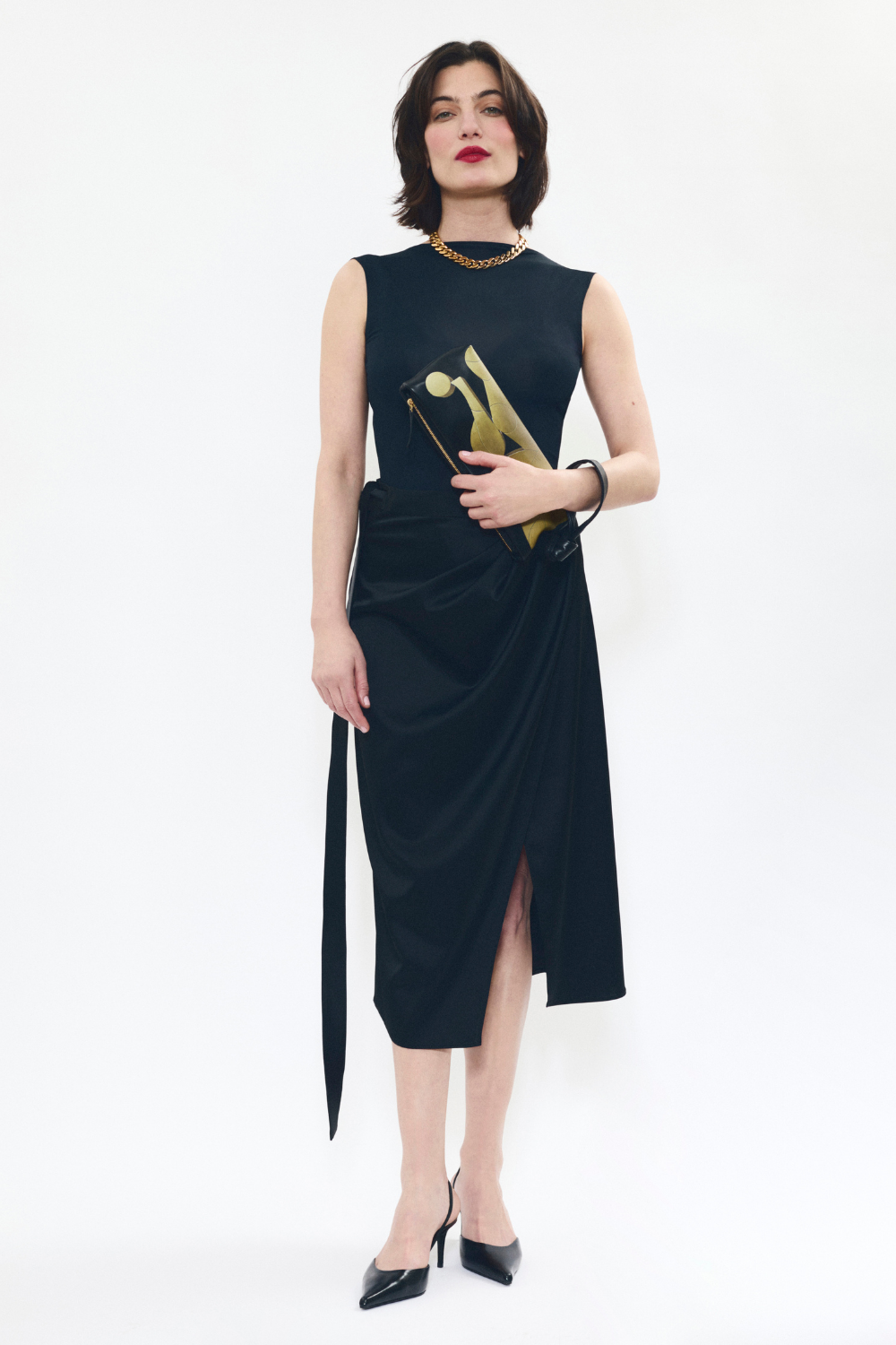 Model holding AYT Studio 'LIEN' elongated black and gold leather pouch with an inspired artistic print and a scarf-inspired wrist strap.