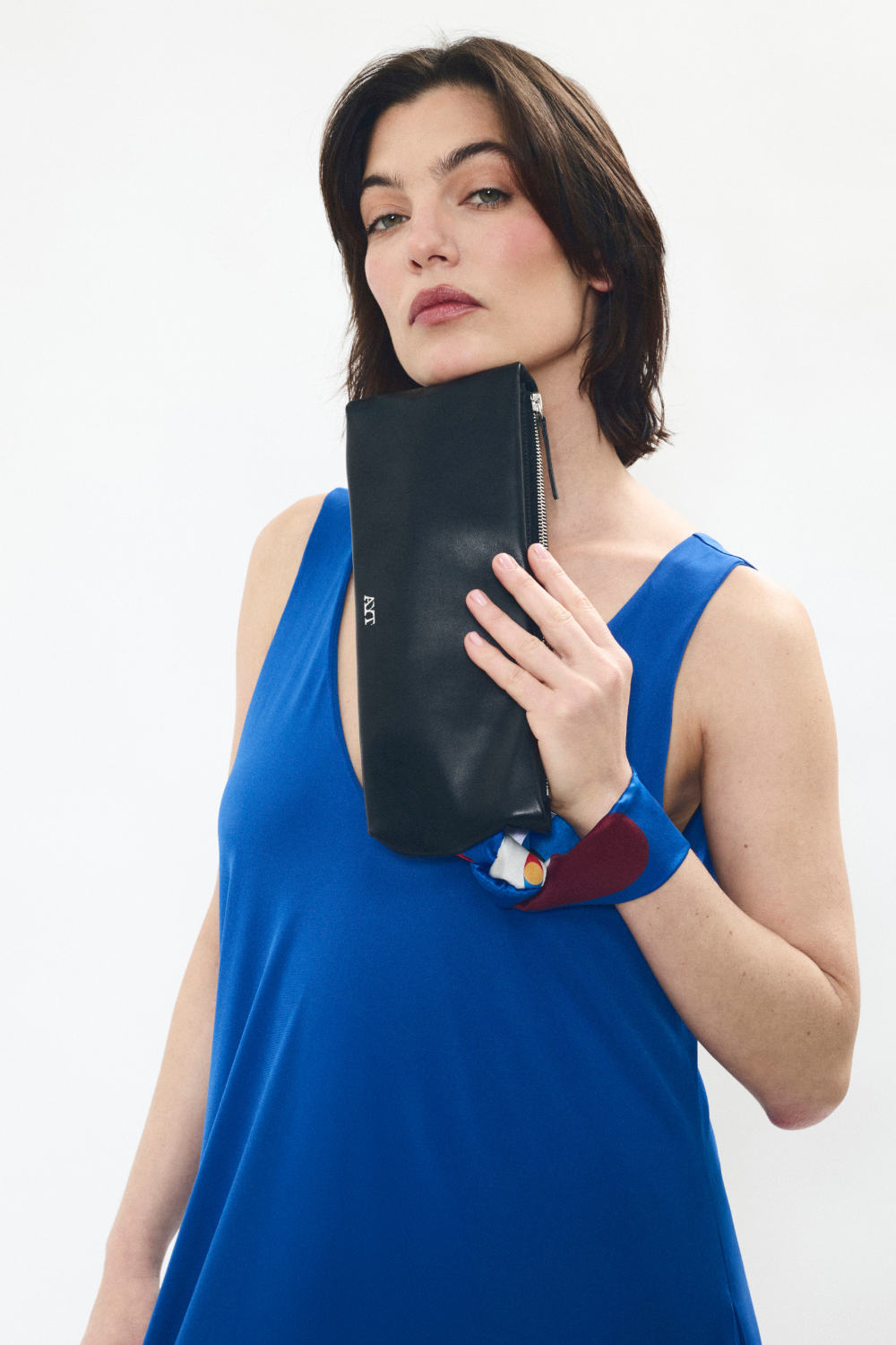Model styling of  AYT Studio 'LIEN' elongated leather pouch, made of smooth black leather with vibrant printed silk wrist strap, limited edition