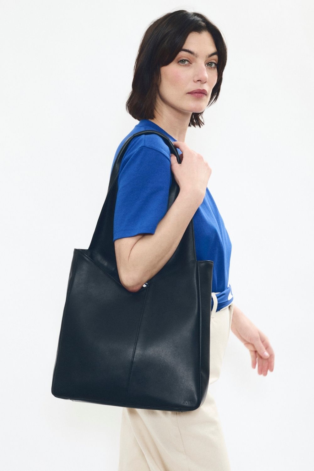 Model wearing AYT Studio 'FOULARD' tote bag made of black Italian leather and lining with zipped interior pocket, metal key hook, and  handle with sophisticated scarf detail