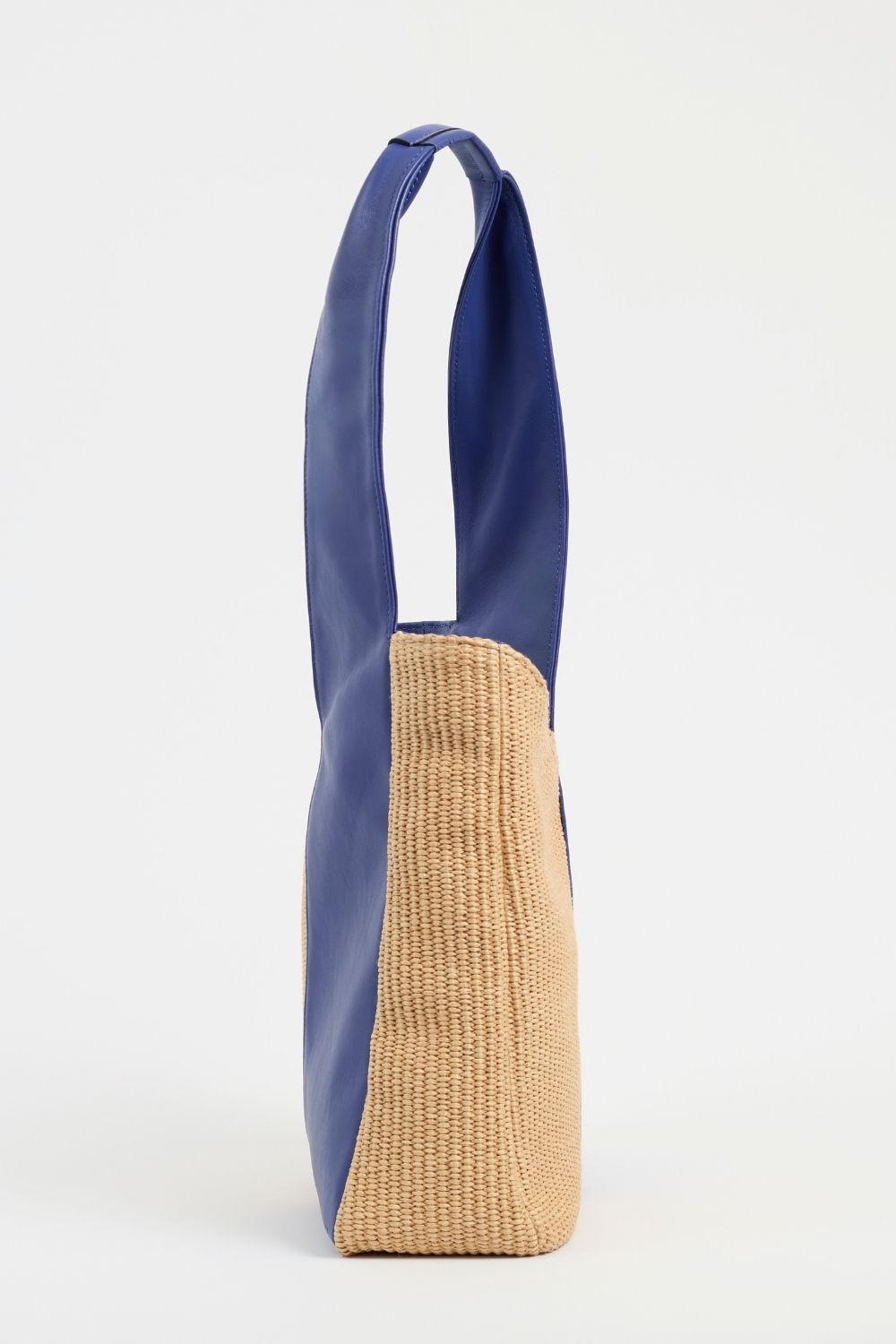 Side view of AYT Studio 'FOULARD' tote bag made of blue leather, natural raffia, and blue canvas lining with zipped interior pocket, metal key hook, and  handle with sophisticated scarf detail