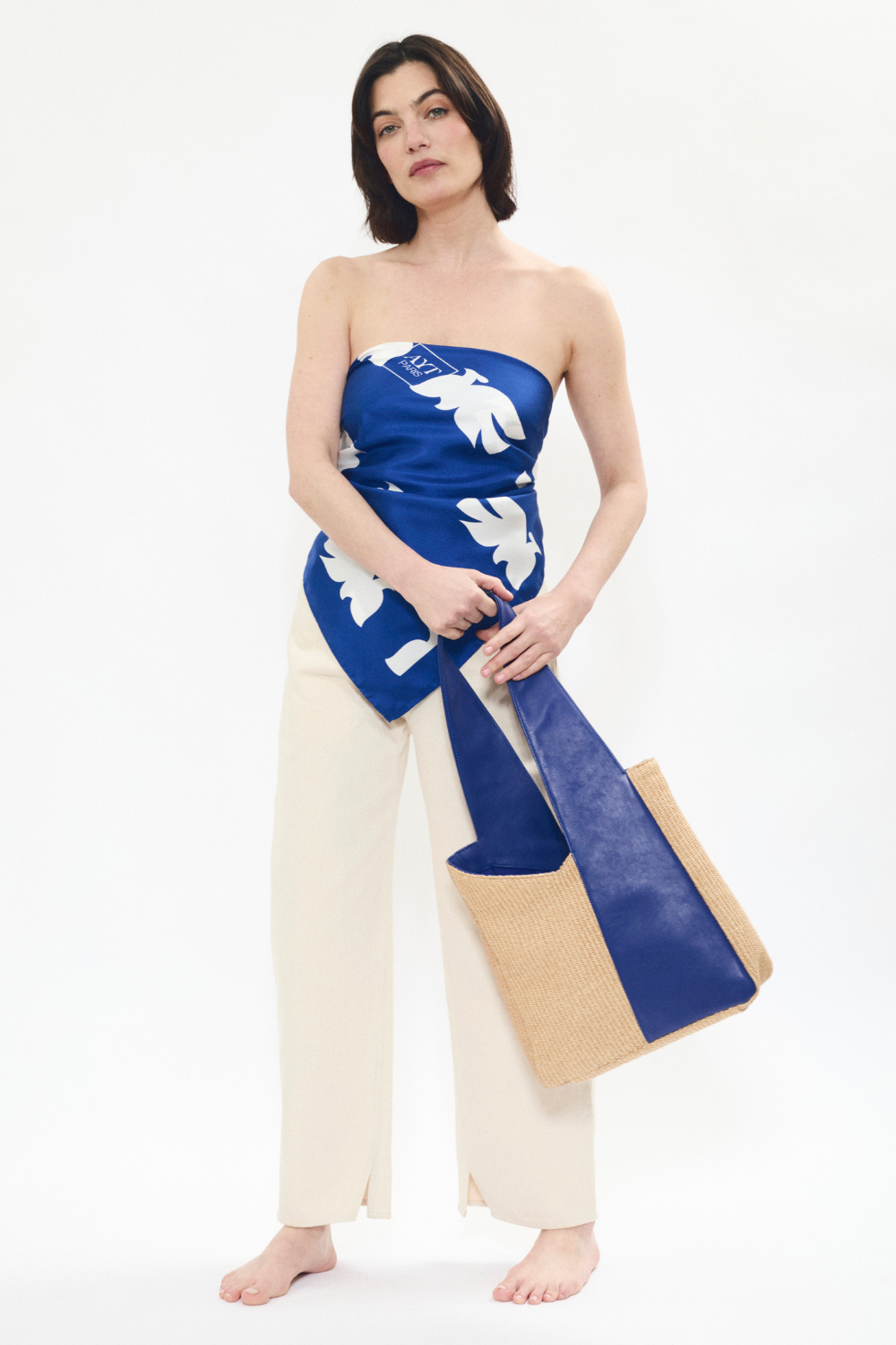 Model holding AYT Studio 'FOULARD' tote bag made of blue leather, natural raffia, and blue canvas lining with handle with sophisticated scarf detail