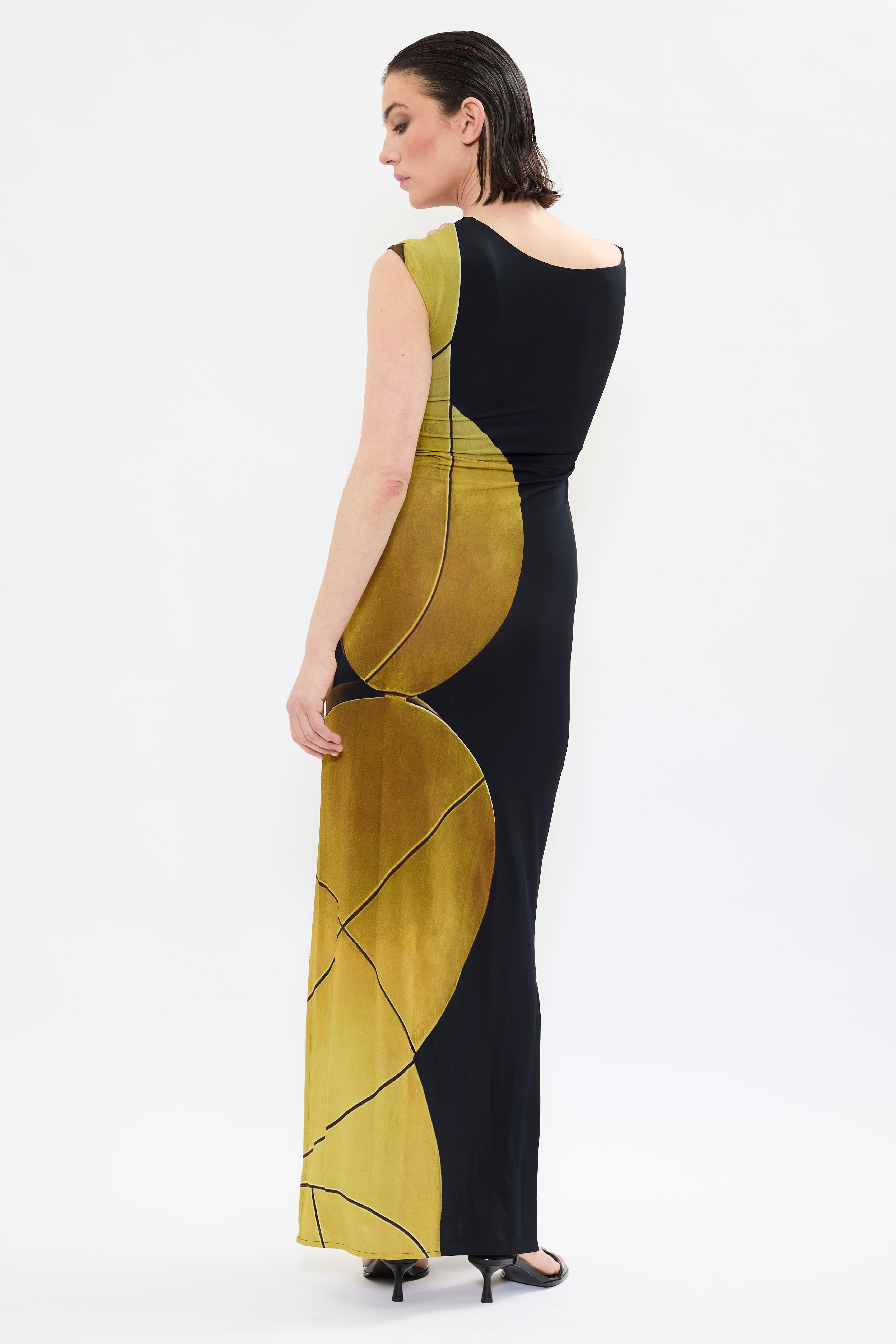 Back ofAYT STUDIO x REMED, 'AURA' fluid viscose and elastane maxi dress with asymmetrical shoulder and side slits in printed black and gold, inspired by 'Femme & sphère.'