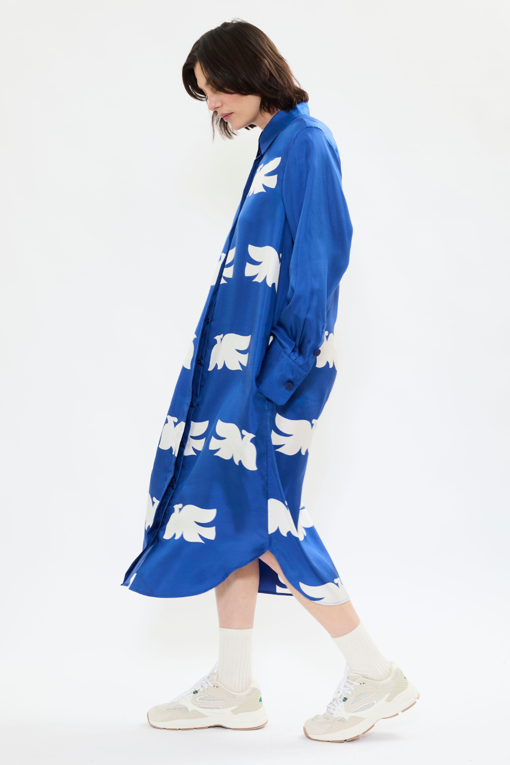 Profile view of AYT Studio x French artist REMED 'CLOUD OF BIRDS' 100% twill silk button shirt dress with structured collar, long sleeves, and discreet pockets. Lightweight and versatile for day-to-night, relaxed, feminine style. Inspired by REMED's 'Bel Envol.'