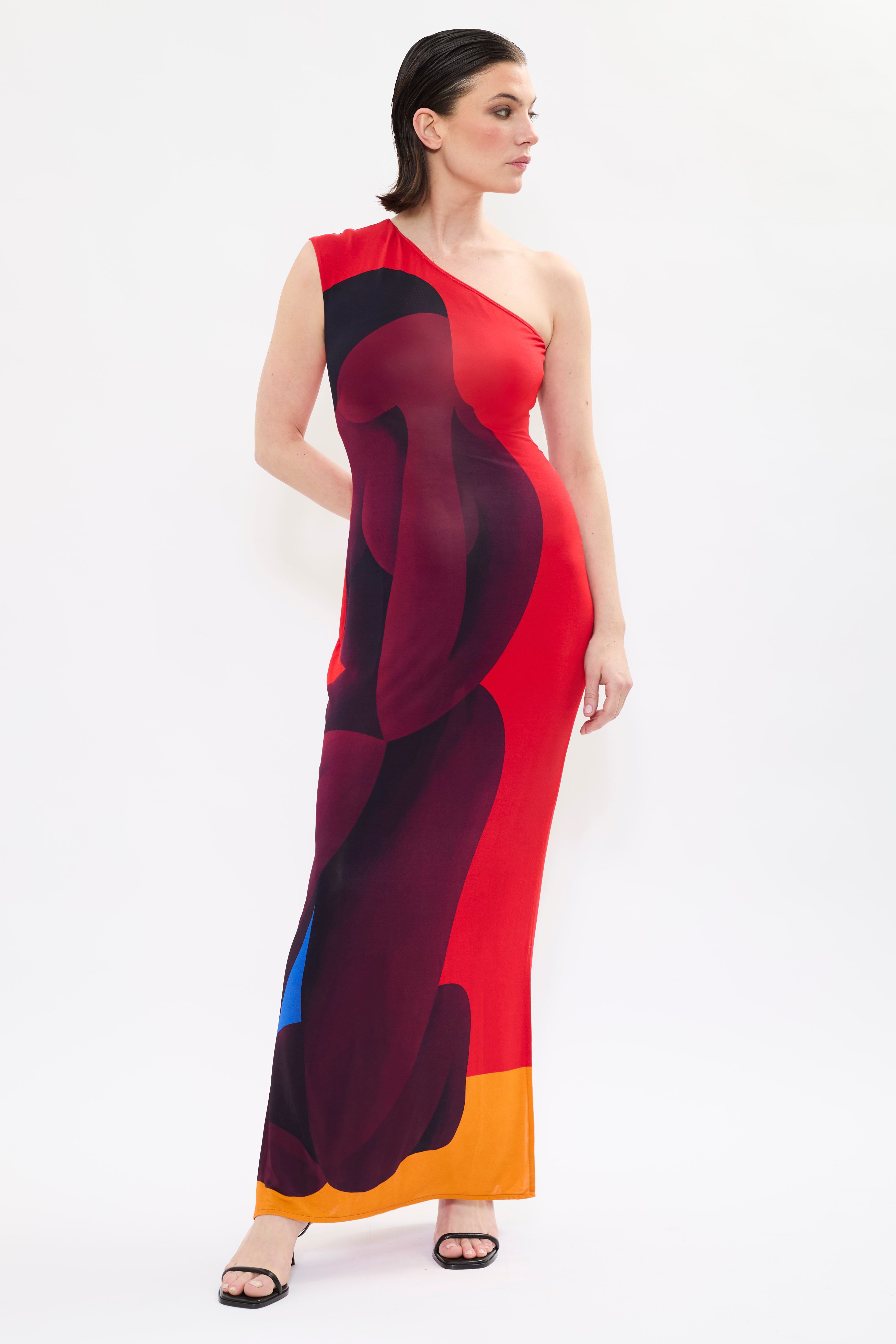 Model in AYT STUDIO x REMED ‘Muse’ one-shoulder maxi dress in fluid viscose with sculptural sleeve and red, black and orange bold artistic print inspired by 'El lago intimo.'