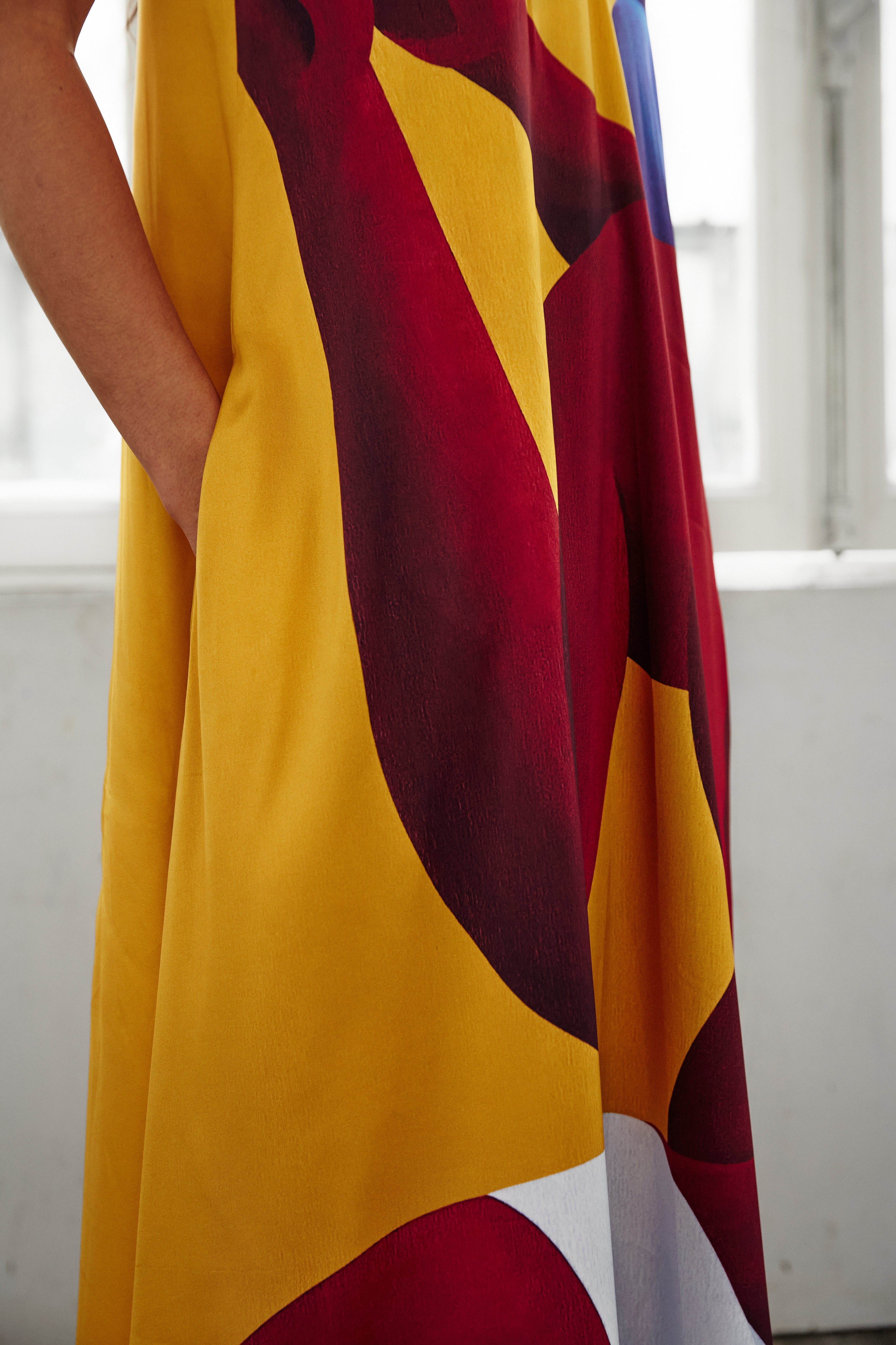Details of AYT Studio x French artist REMED 'SORORITY' fluid, vibrant yellow printed dress in viscose and elastane with punging V-neck front and back and discreet side pockets. Inspired by REMED's 'Bain de sable.'