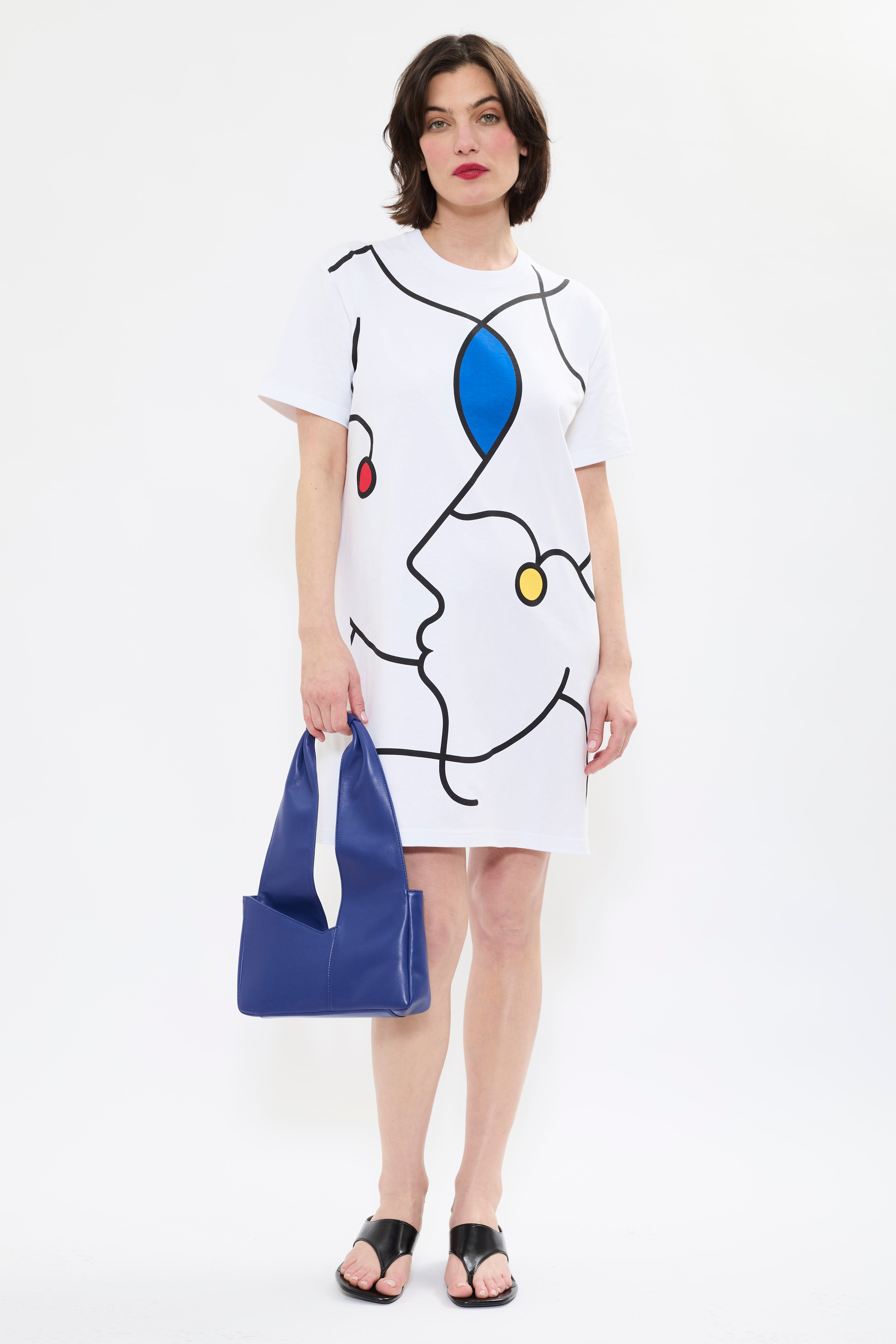 Model holding AYT Studio x Remed white organic cotton T-shirt dress with line-art print and a straight, oversized fit styled with AYT Studio 'DUAL' shoulder bag.