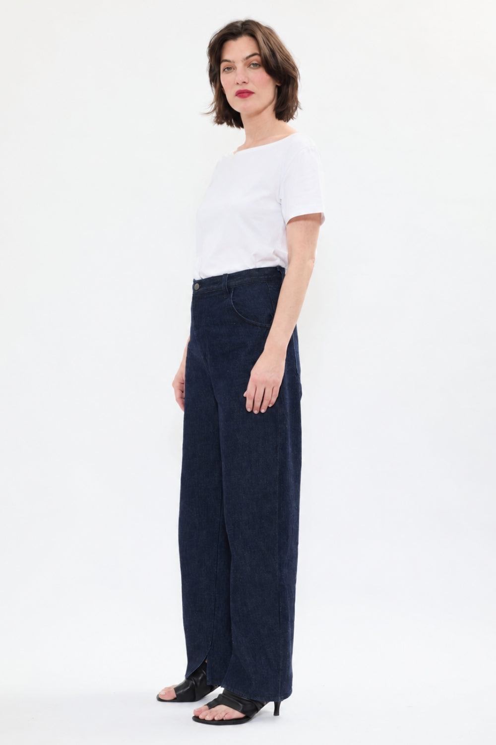 Side view of AYT STUDIO 'TRIBE' high-rise curved straight leg 100% recycled cotton jeans in blue with signature AYT Studio logo, ankle slit detail, and functional front and back pockets.